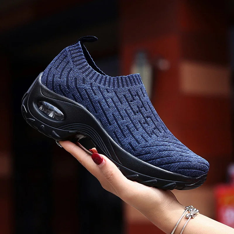 a woman's hand holding a blue knitted sneaker