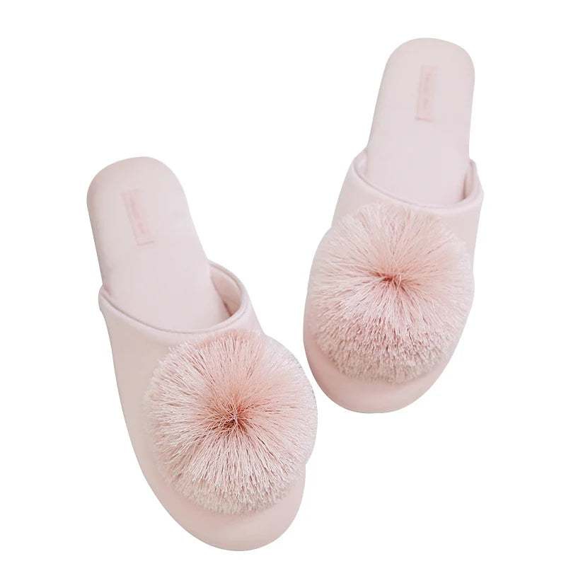 a pair of pink slippers with pom poms