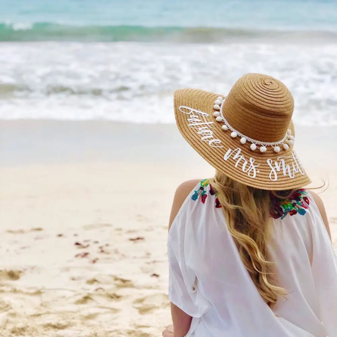 a woman sitting on a beach wearing a straw hat