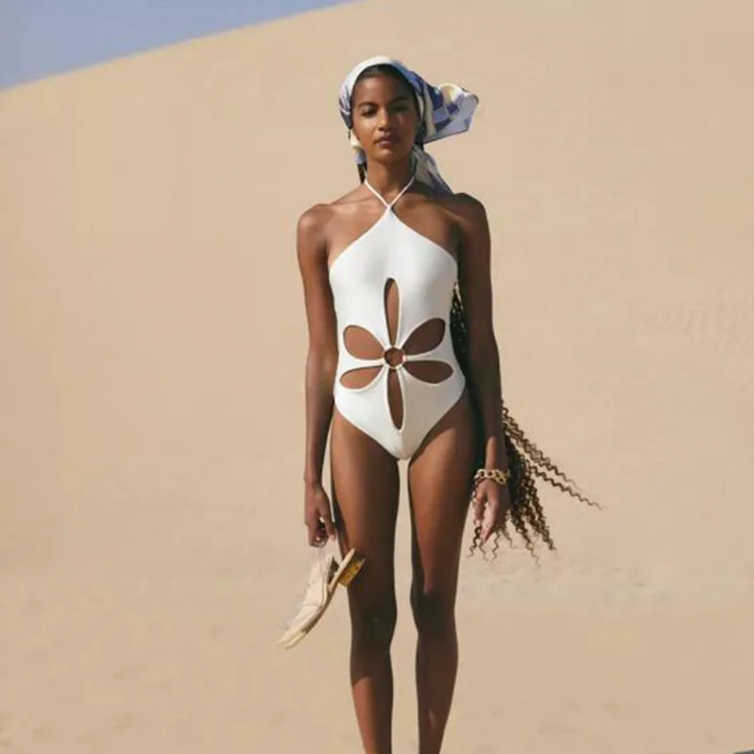 a woman in a white one piece swimsuit walking in the sand